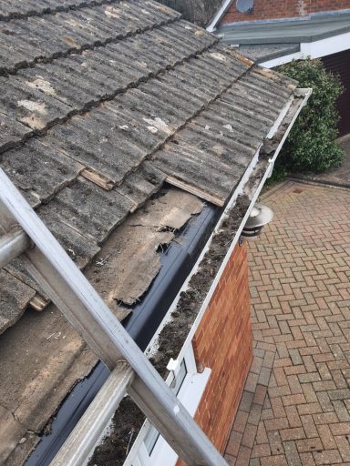 Close-up of a roof showing worn tiles and debris in the gutter.
