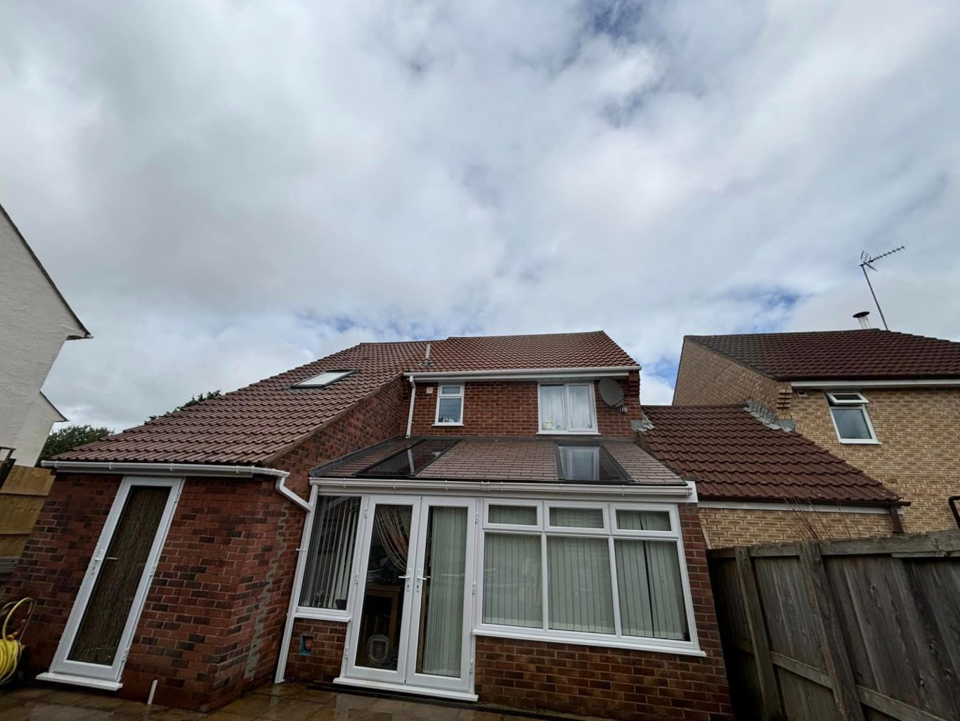 Roof Cleaning Two-storey brick house with a conservatory and cloudy sky in the background.