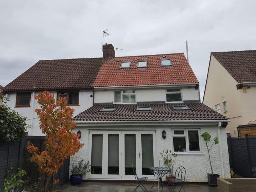 Two-storey house with a red roof, white walls, and a garden with a decorative tree.