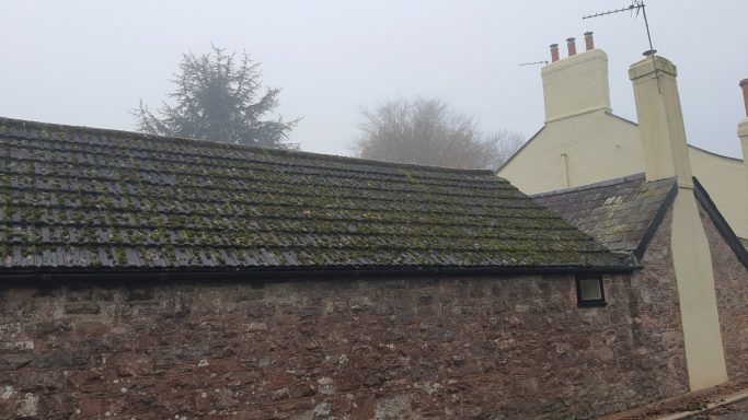 A foggy scene featuring two buildings with textured stone walls and mossy roofs.