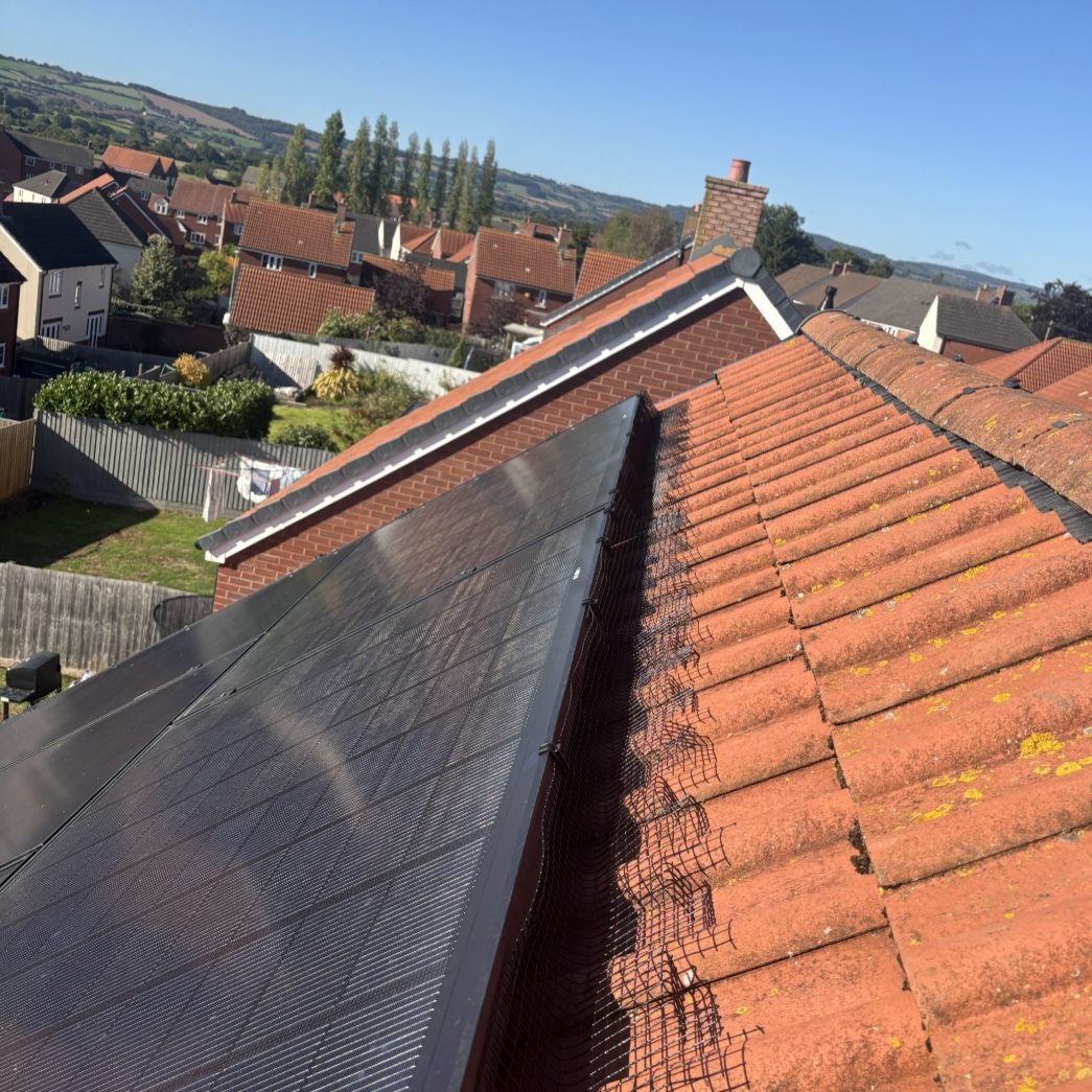 Solar panels on a roof with a box and debris near the edge of the gutter.