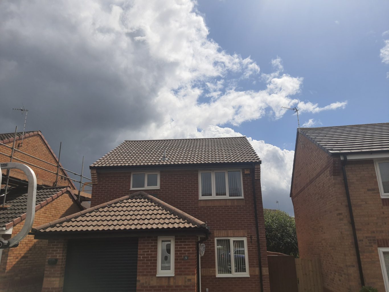 Roof Cleaning A brick house with a tiled roof under a partly cloudy sky.