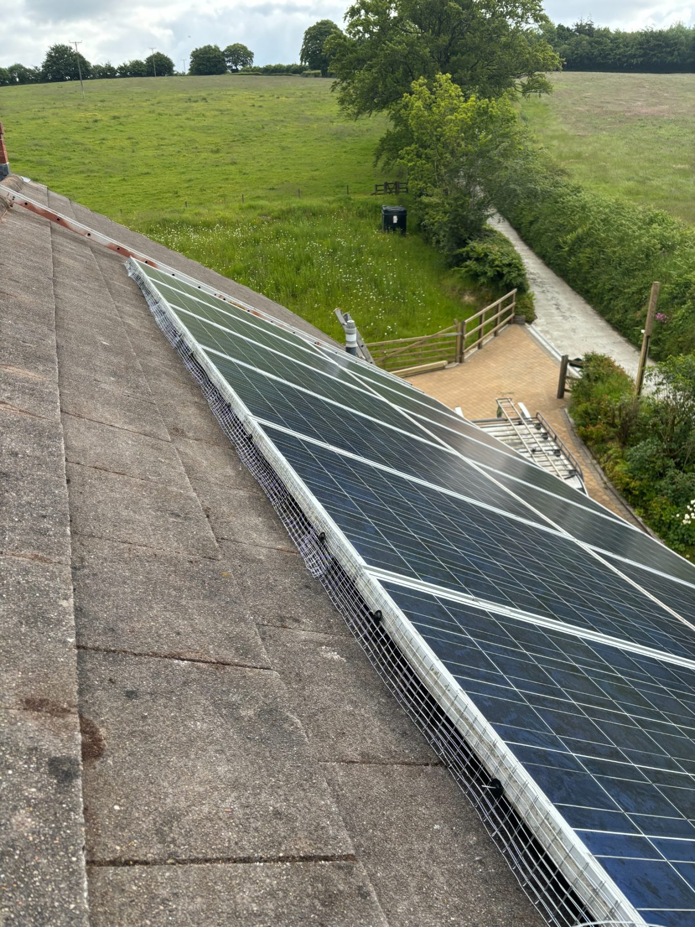 Solar Panel protection installation Solar panels installed on a roof, overlooking a green field and pathway.
