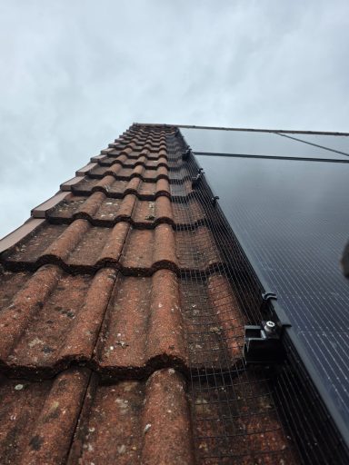 Solar panel Protection In Bristol View of a roof with red tiles and a solar panel against a cloudy sky.