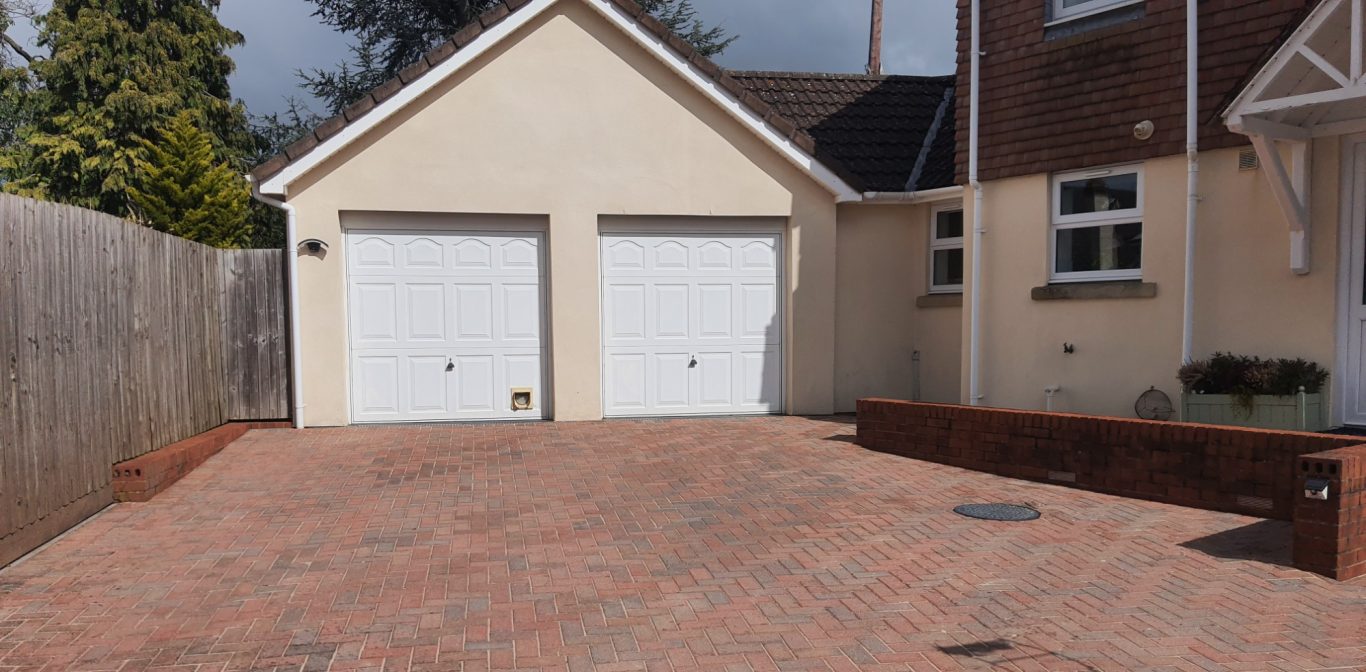 Driveway cleaning A driveway with red brick paving leading to a double garage with white doors.