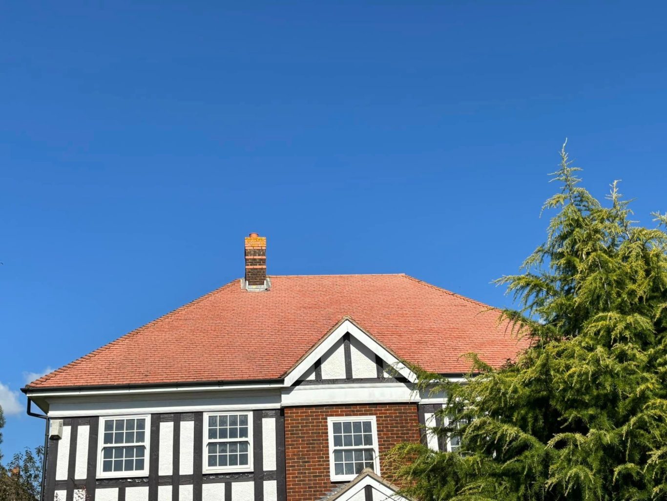 Roof Cleaning After. Roof of a traditional house with a chimney against a clear blue sky.
