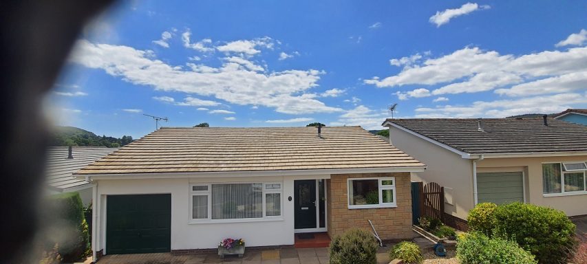 Bungalow house with a front garden under a blue sky with scattered clouds.