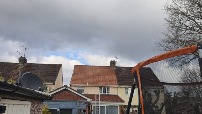 Houses with cloudy sky, a trampoline in the foreground.