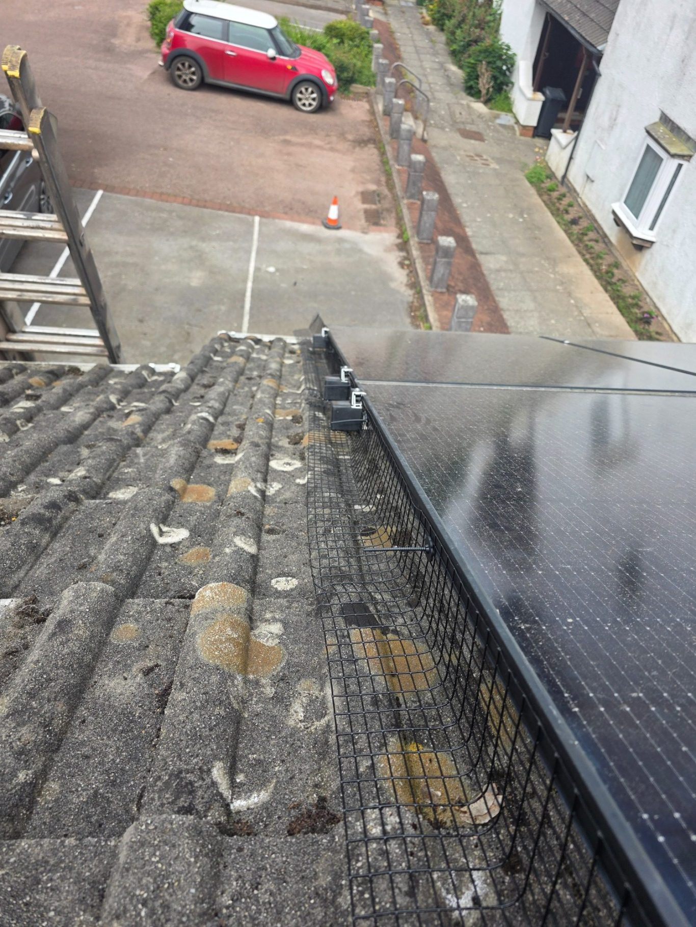 Solar panel mesh installation Devon View from a rooftop showing solar panels and a car parked nearby.