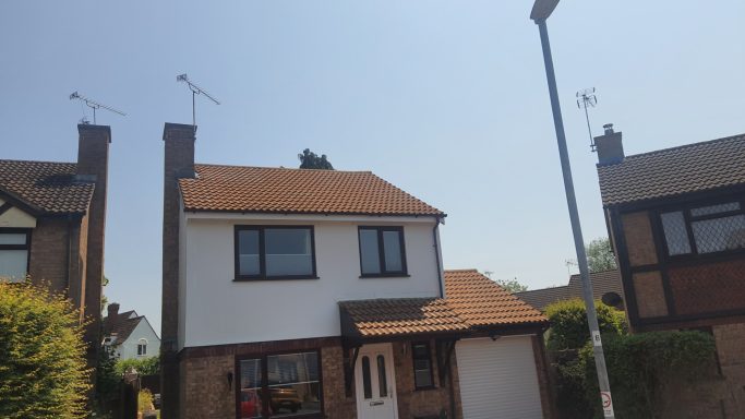 Two-storey detached house with a brown roof and white walls, set against a clear blue sky.