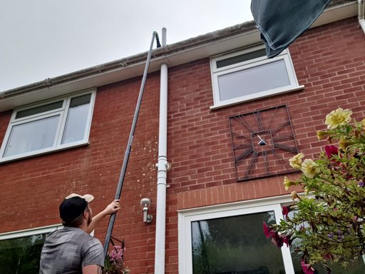 A person uses a long pole to reach the roof of a red-brick house.