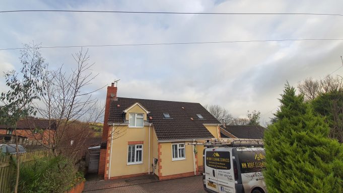 A two-storey yellow house with a grey roof and surrounding greenery.