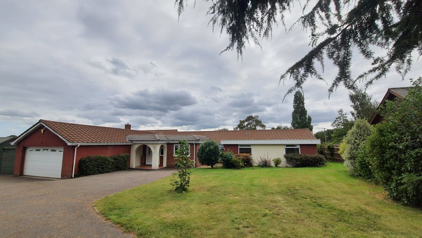 Roof cleaning Single-story red brick house with a front lawn and cloudy sky.