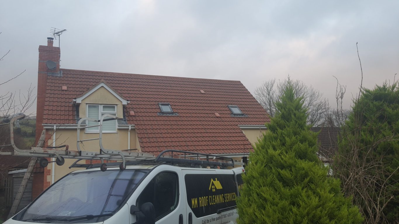 Roof Cleaning A van parked in front of a house with a red tiled roof and cloudy sky above.