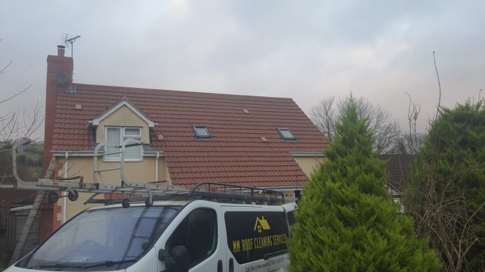 A van parked in front of a house with a red tiled roof and cloudy sky above.