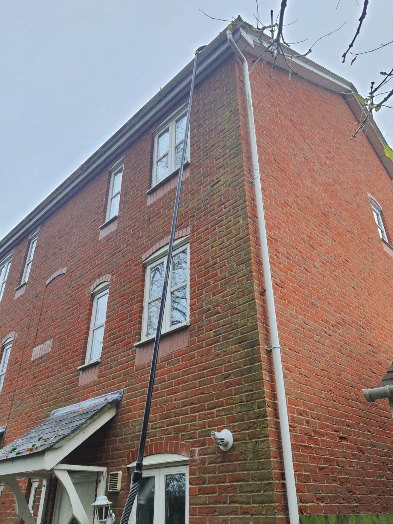 Gutter Vacuuming A brick building with a long black hose extending from the roof.