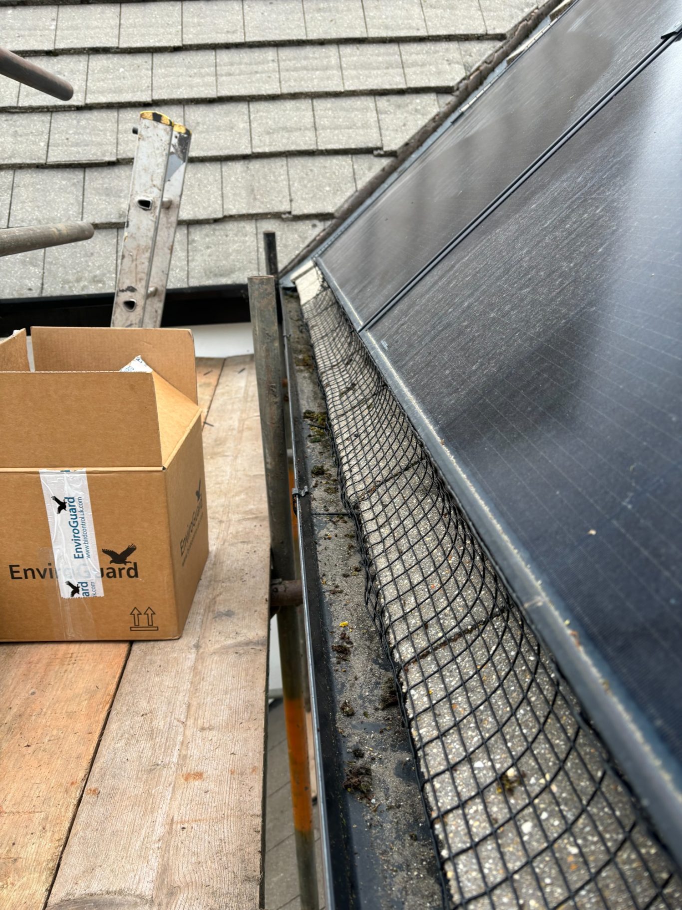 Solar Panel protection installation. Box next to solar panels on a roof, with a ladder in the background.